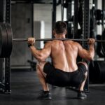 Athlete de dos executant un squat barre chargee en salle de musculation